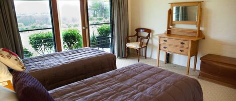 Habitación de hotel con dos camas, un aparador de madera, una silla y un ventanal con vistas a la vegetación.