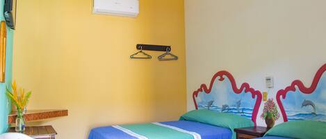 Habitación de hotel con dos camas, una mesita, una silla, un equipo de aire acondicionado y un mural en la pared.