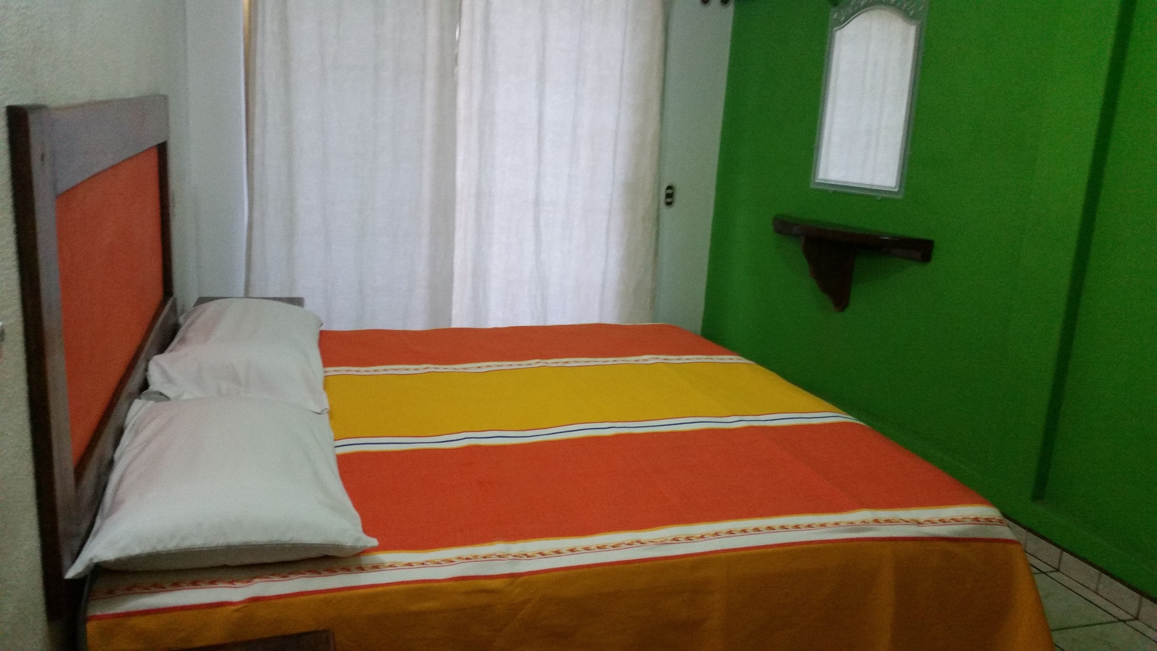 A small, narrow room with a bed, a window, and a green door.