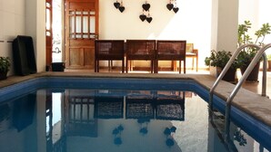 Zona de piscina con suelo de baldosas, sillas y mesa de madera, y una pared decorada con corazones.