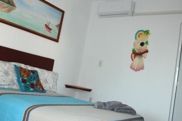 Un dormitorio con cama, almohadas, un adorno en la pared y una pequeña estantería.
