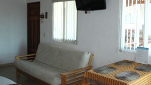Una habitación con un sofá, un televisor montado en la pared y una mesa con mantel a rayas.