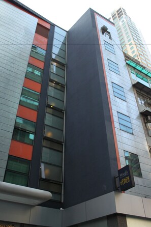 A modern building with a prominent vertical black and red facade, large windows, and a sign indicating a hotel. - Mingle Place At The Eden (Hong Kong)