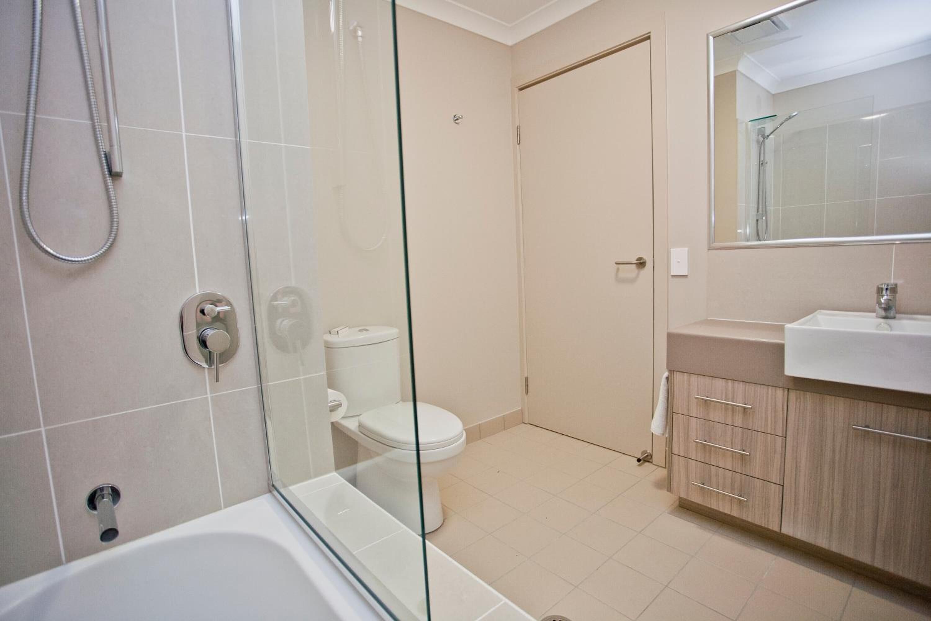 A modern bathroom with a glass-enclosed shower, a white toilet, and a beige vanity with a mirror.