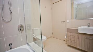 A modern bathroom with a glass-enclosed shower, a white toilet, and a beige vanity with a mirror.