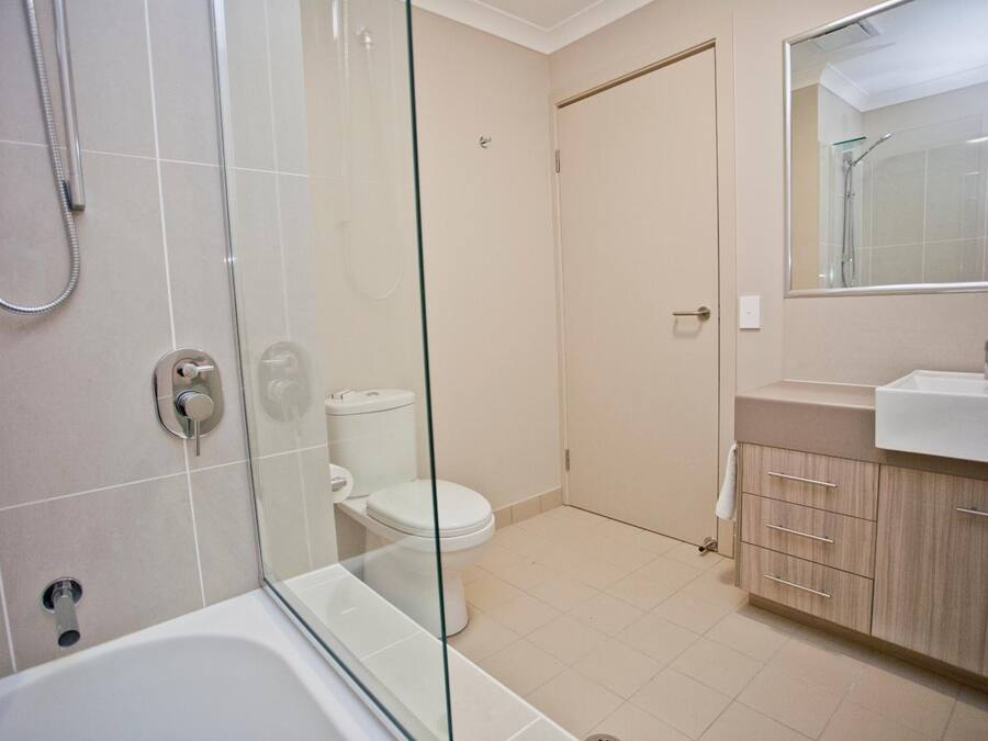 A modern bathroom with a glass-enclosed shower, a white toilet, and a beige vanity with a mirror.