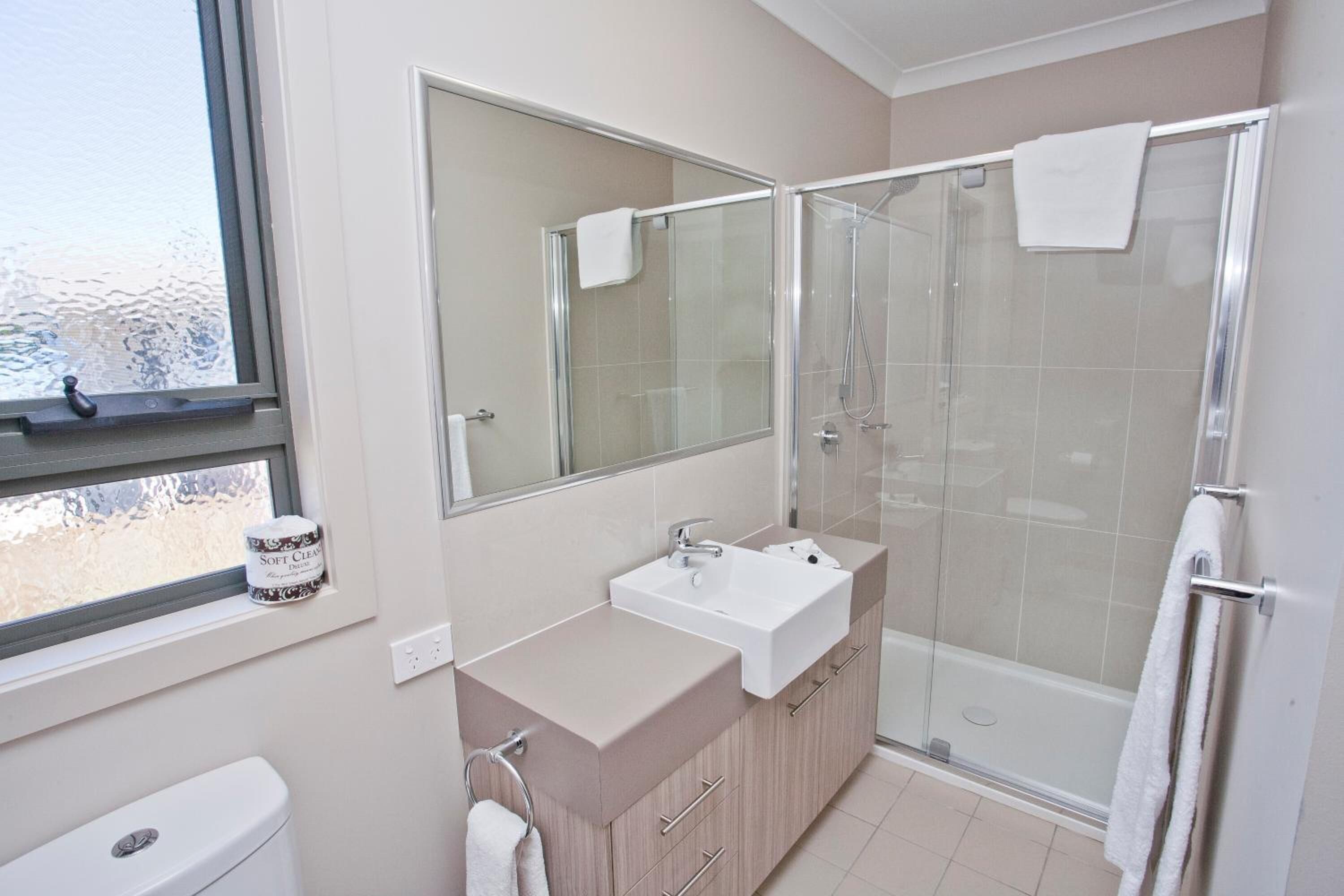 A bathroom with a toilet, a sink, a mirror, and a glass-enclosed shower.