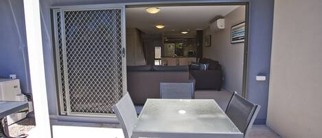 Un patio con una mesa y sillas de vidrio, una puerta corrediza y vistas a una cocina y sala de estar.