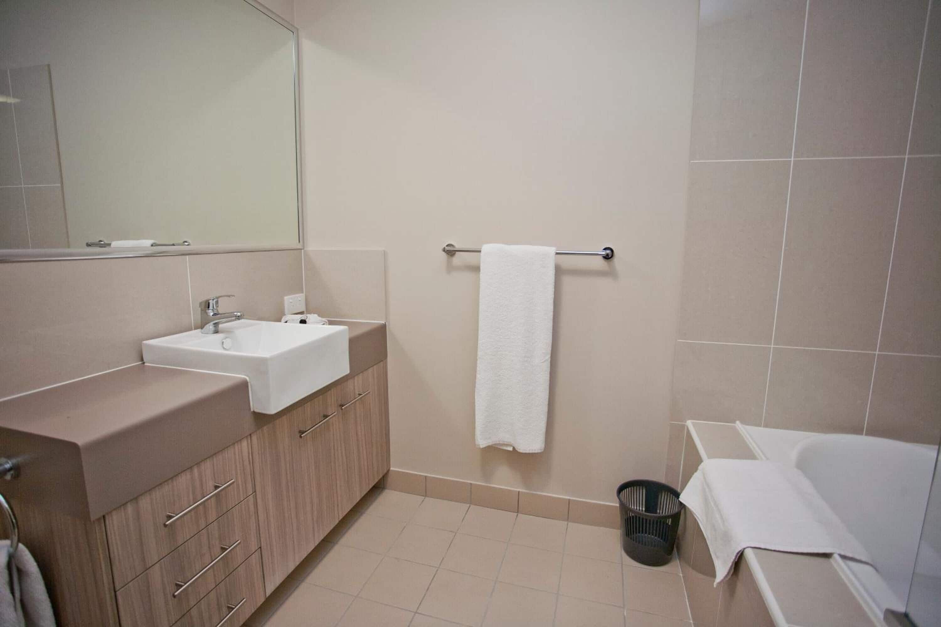 Un baño moderno con lavamanos, espejo, toallero y bañera.