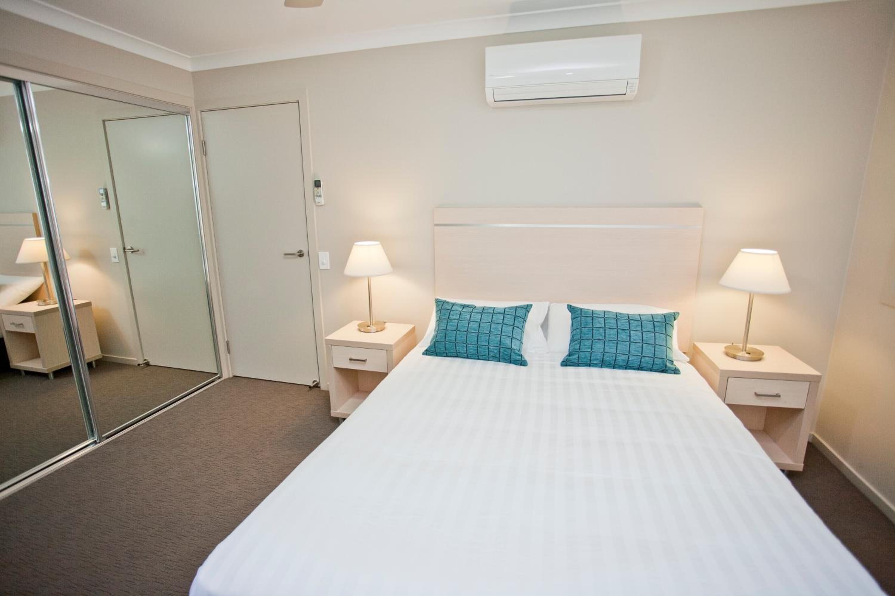 Habitación de hotel con una cama grande, dos mesitas de noche con lámparas, un espejo y un aire acondicionado instalado en la pared.