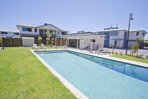 A swimming pool with a grassy area, a covered patio, and a two-story building with balconies. - Stonewood Villas (Chinchilla)