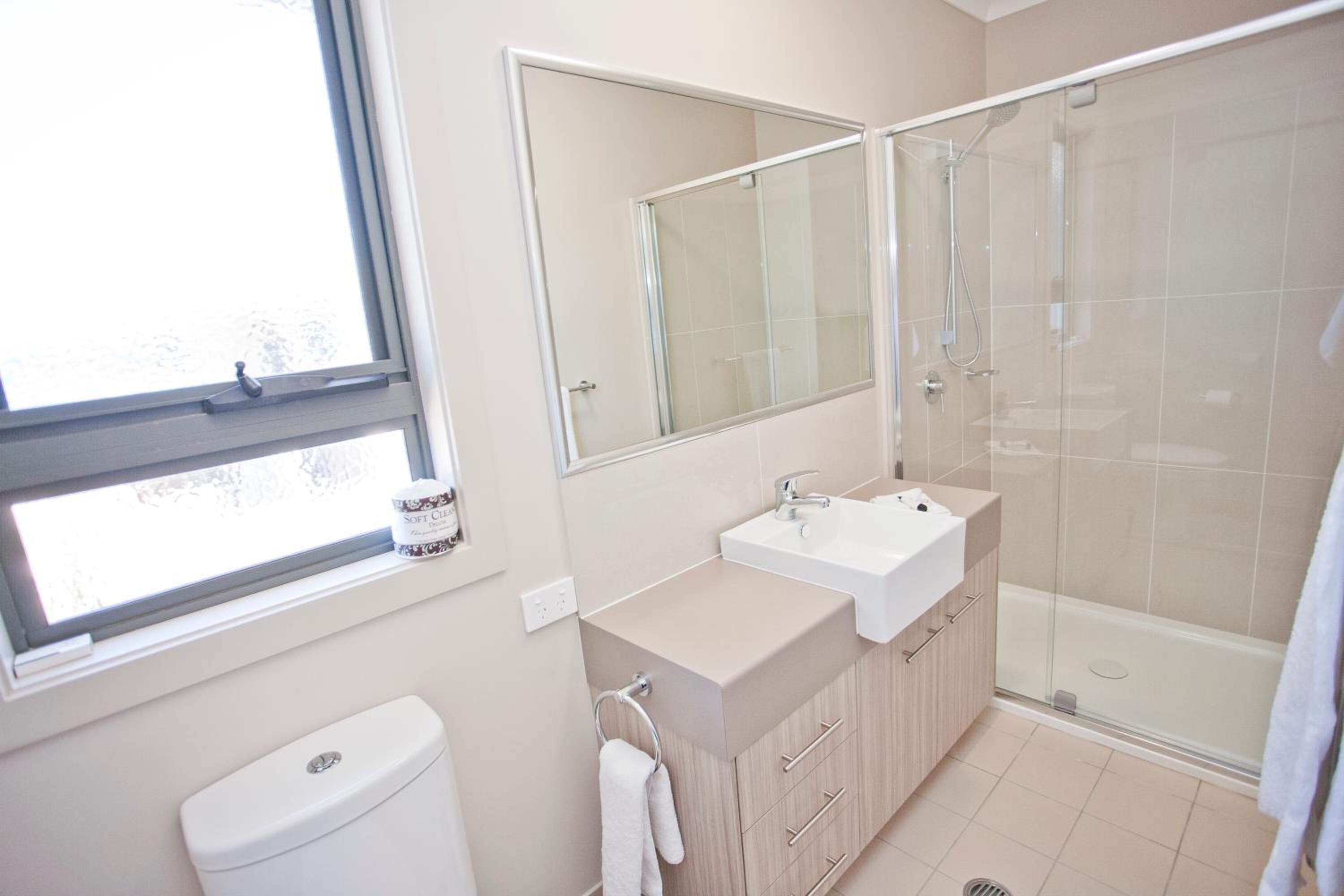 Une salle de bain moderne équipée de toilettes, d’un lavabo, d’un miroir et d’une douche.