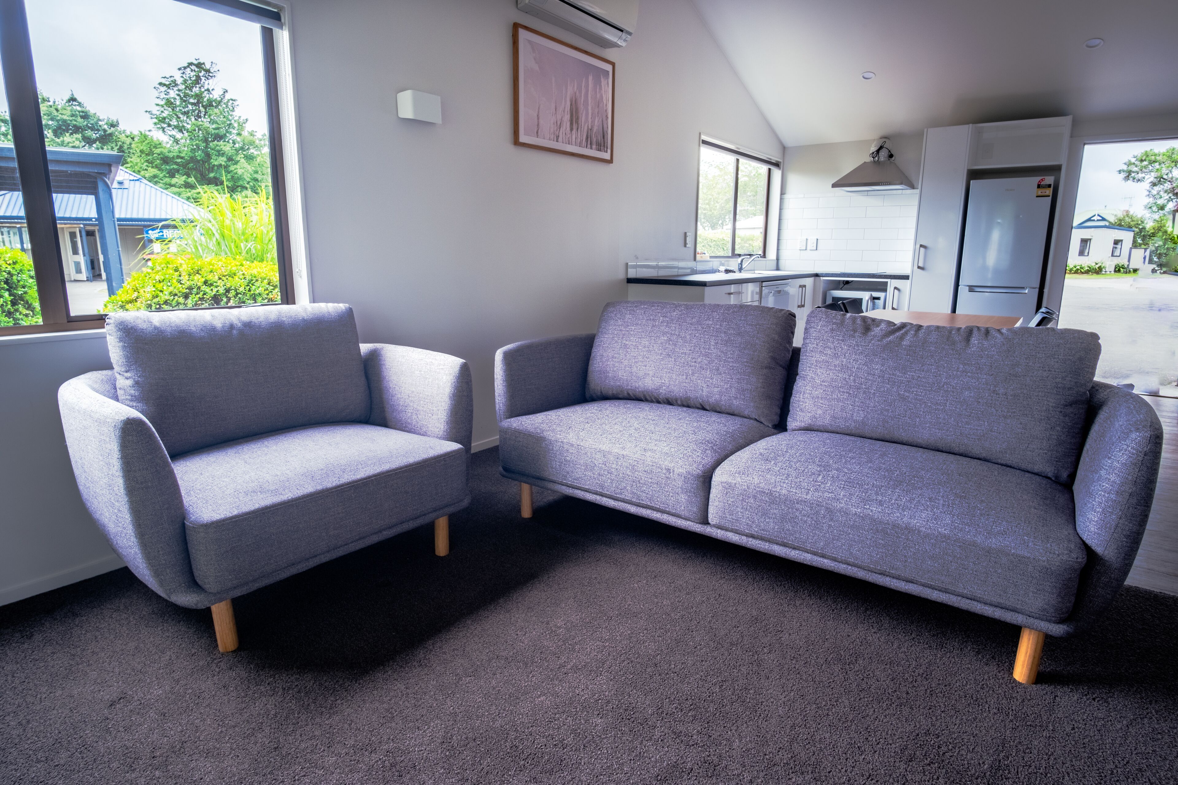 A modern living room with two grey sofas and a kitchen in the background.