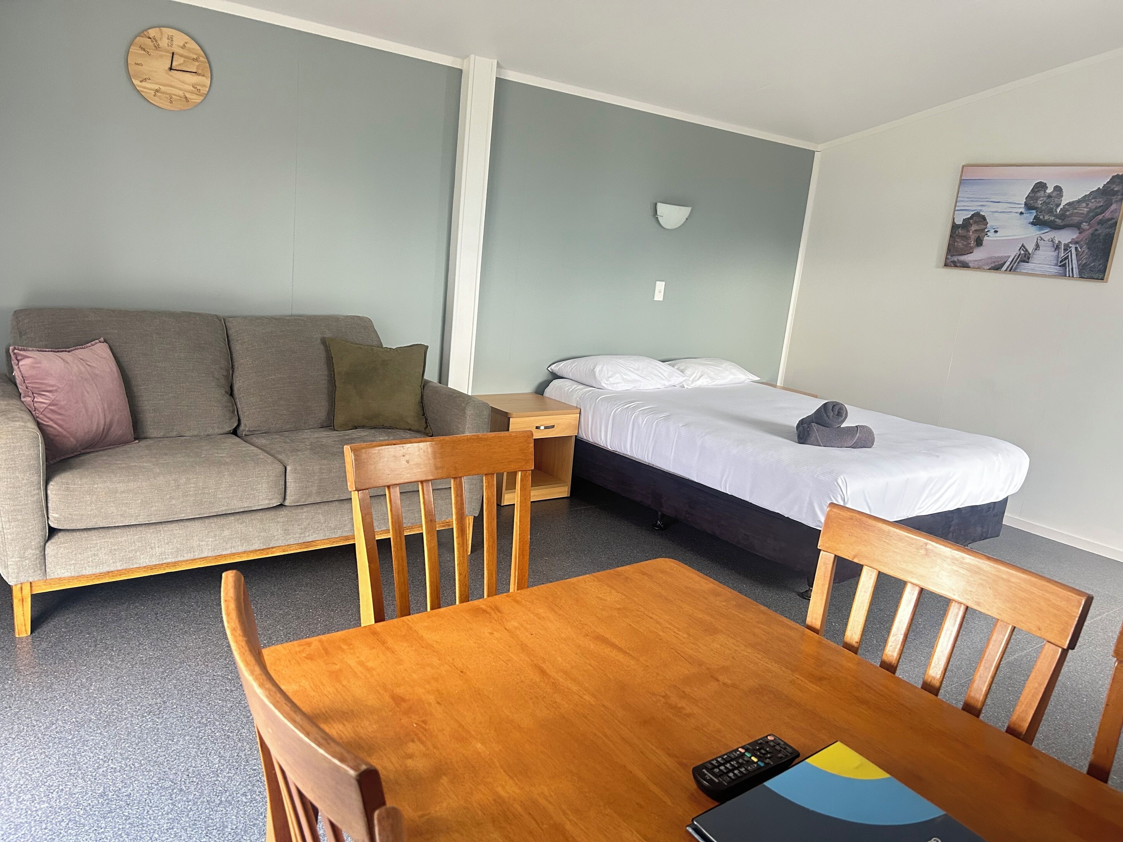 Ein Zimmer mit einer Couch, einem Bett, einem Holztisch und einer Wanduhr.