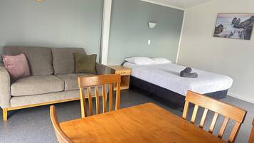 Ein Zimmer mit einer Couch, einem Bett, einem Holztisch und einer Wanduhr.