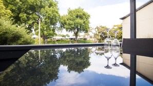 Une table en verre sur laquelle reposent deux verres à vin, et qui reflète clairement les arbres et un bâtiment.