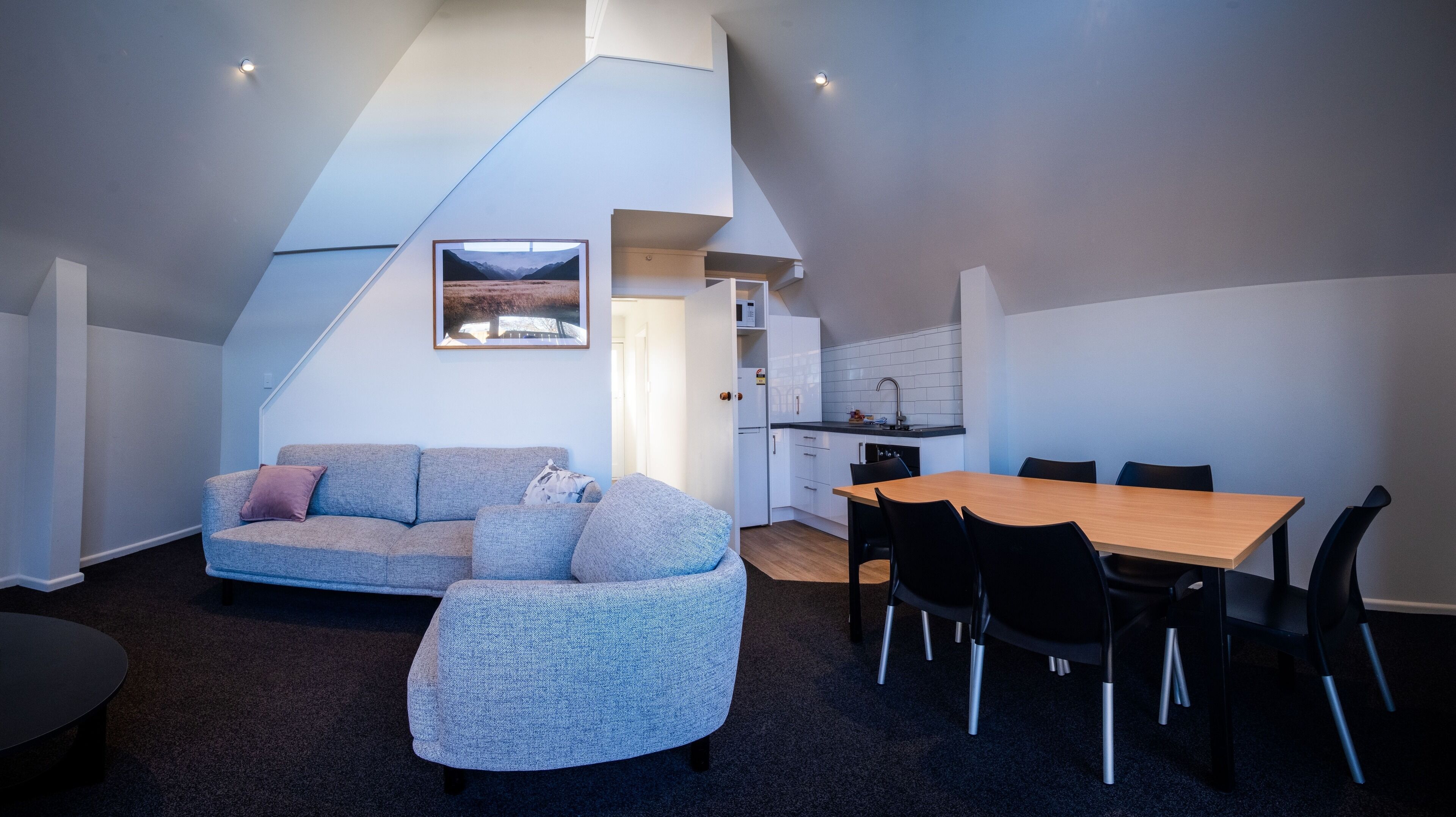 A compact living space with a sofa, a dining table with chairs, a kitchen area, and a staircase leading to an upper level.