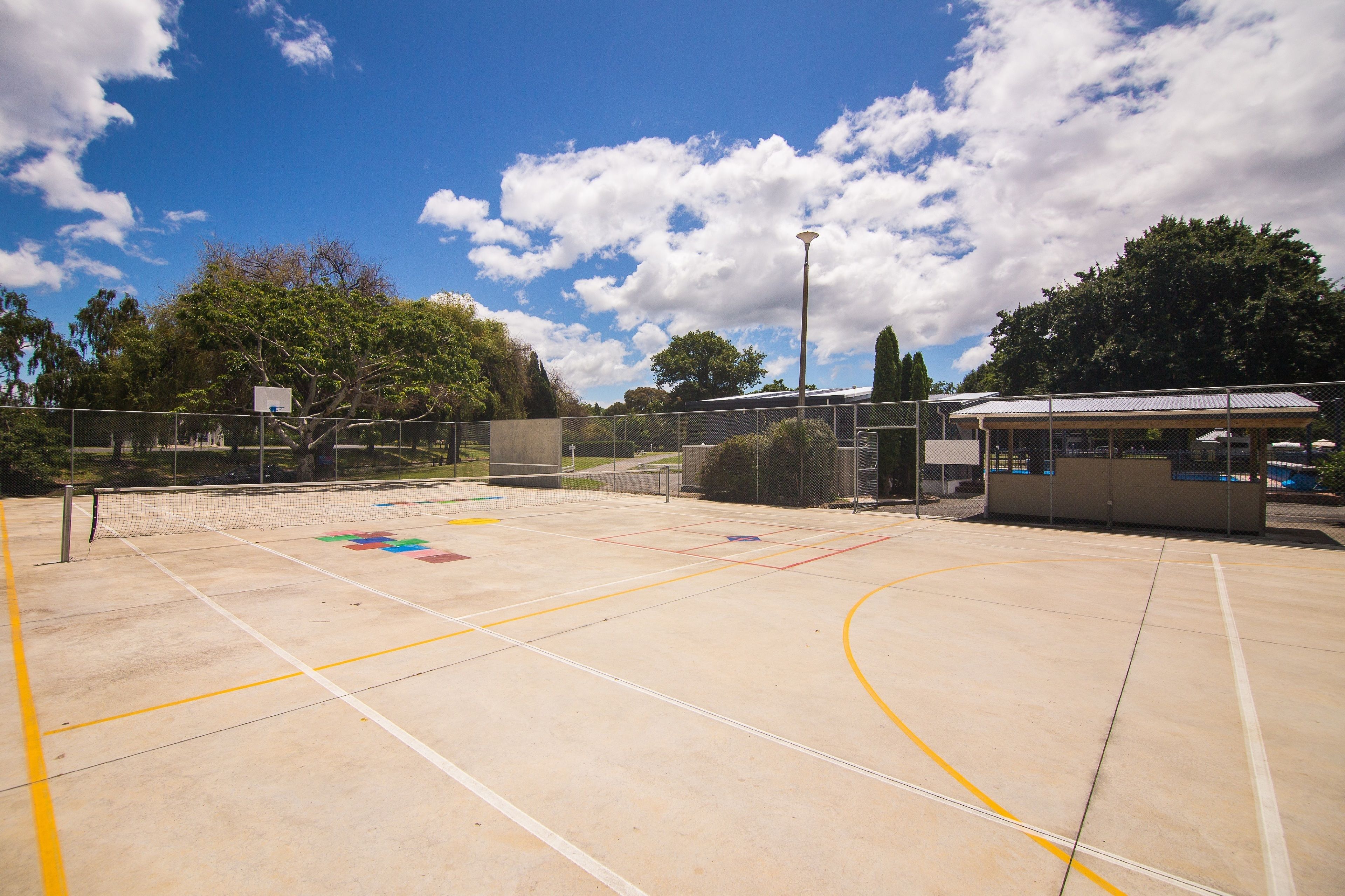Ein Basketballplatz im Freien mit Zaun, Korb und überdachtem Sitzbereich.
