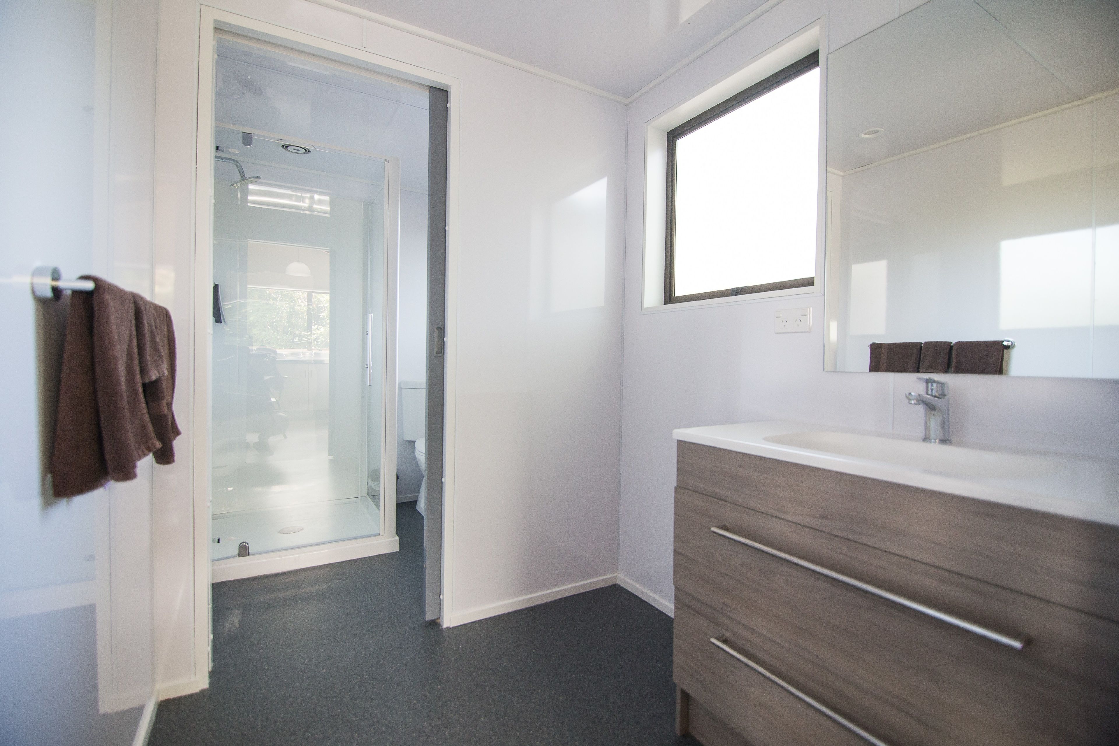 A modern bathroom with a glass shower door, a large mirror, and a wooden vanity.
