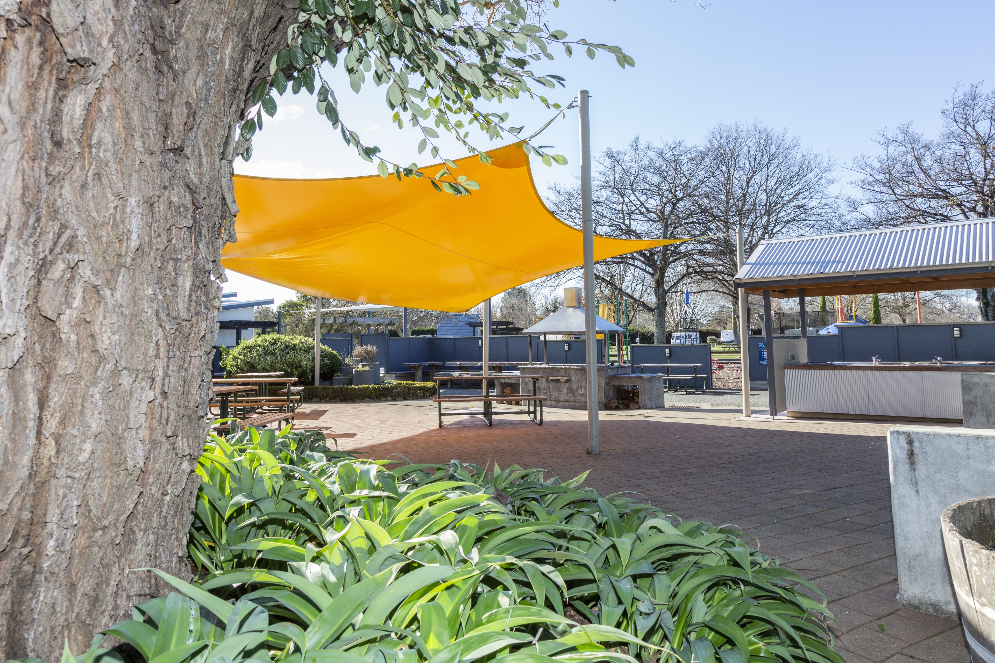 A covered outdoor seating area with benches and a yellow shade sail.