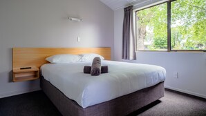 Un lit bien fait, avec du linge de lit blanc, une tête de lit en bois et une moquette gris foncé.