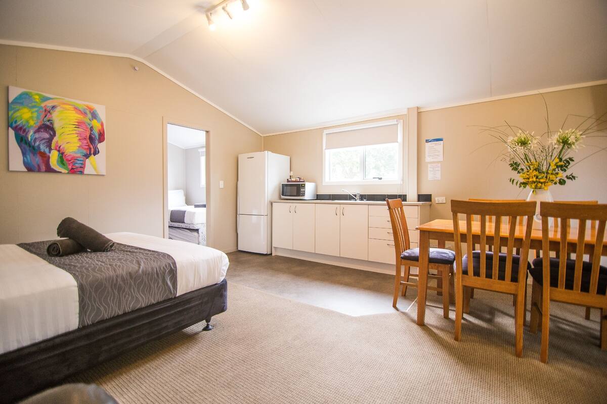 Een slaapkamer met een bed, een eettafel met stoelen, een magnetron en een koelkast.