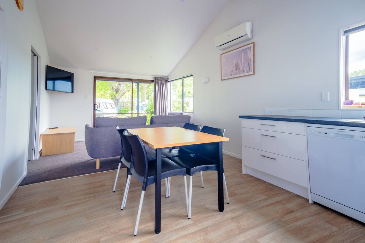 Een moderne keuken met een houten tafel en stoelen, een inbouw vaatwasser en een groot raam met uitzicht op de omgeving.