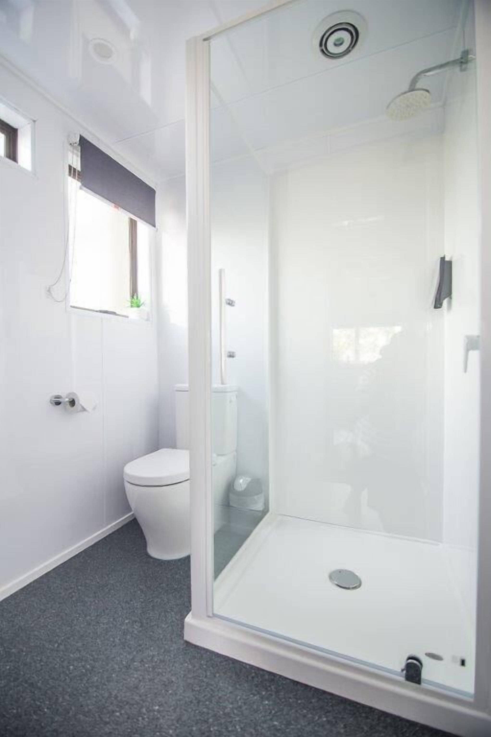A modern bathroom with a glass-enclosed shower, a toilet, and a window.