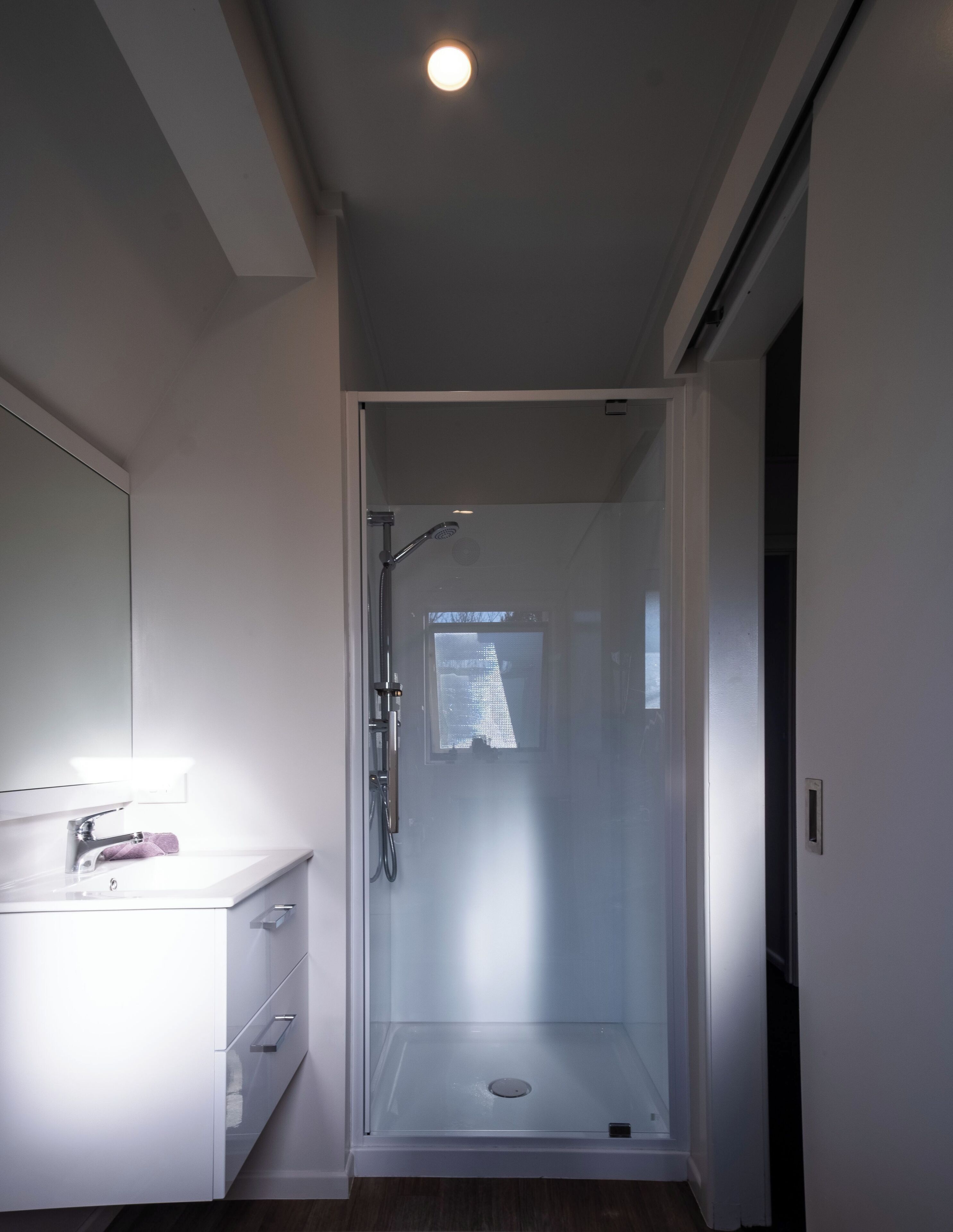 A modern bathroom with a glass-enclosed shower, a white vanity with a mirror, and a recessed ceiling light.