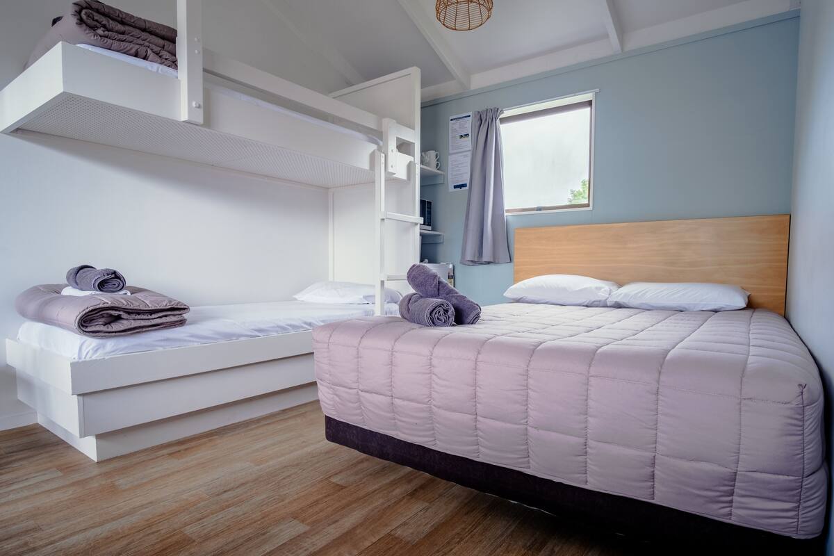 Een kamer met een stapelbed, een enkel bed, houten vloeren, een raam met gordijnen en een plafondlamp.