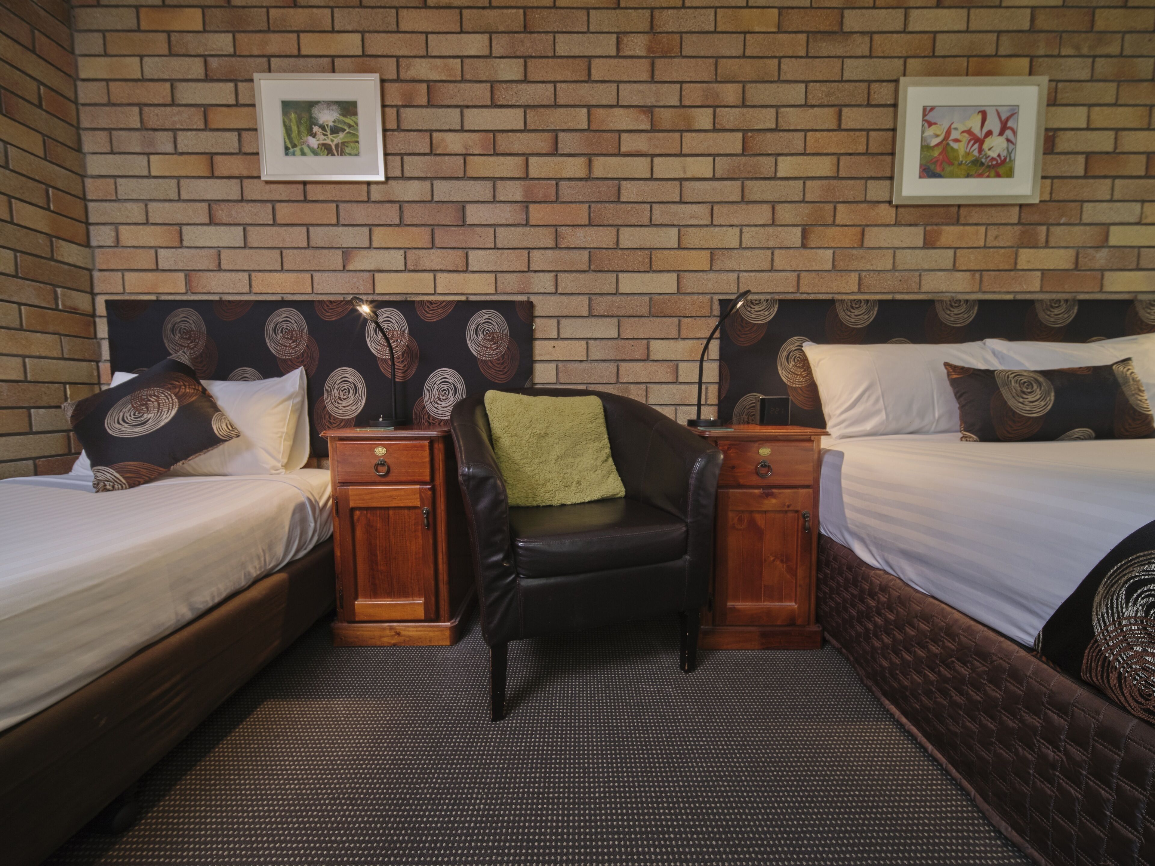 A hotel room with two beds, a small sofa, and a brick-patterned wall.