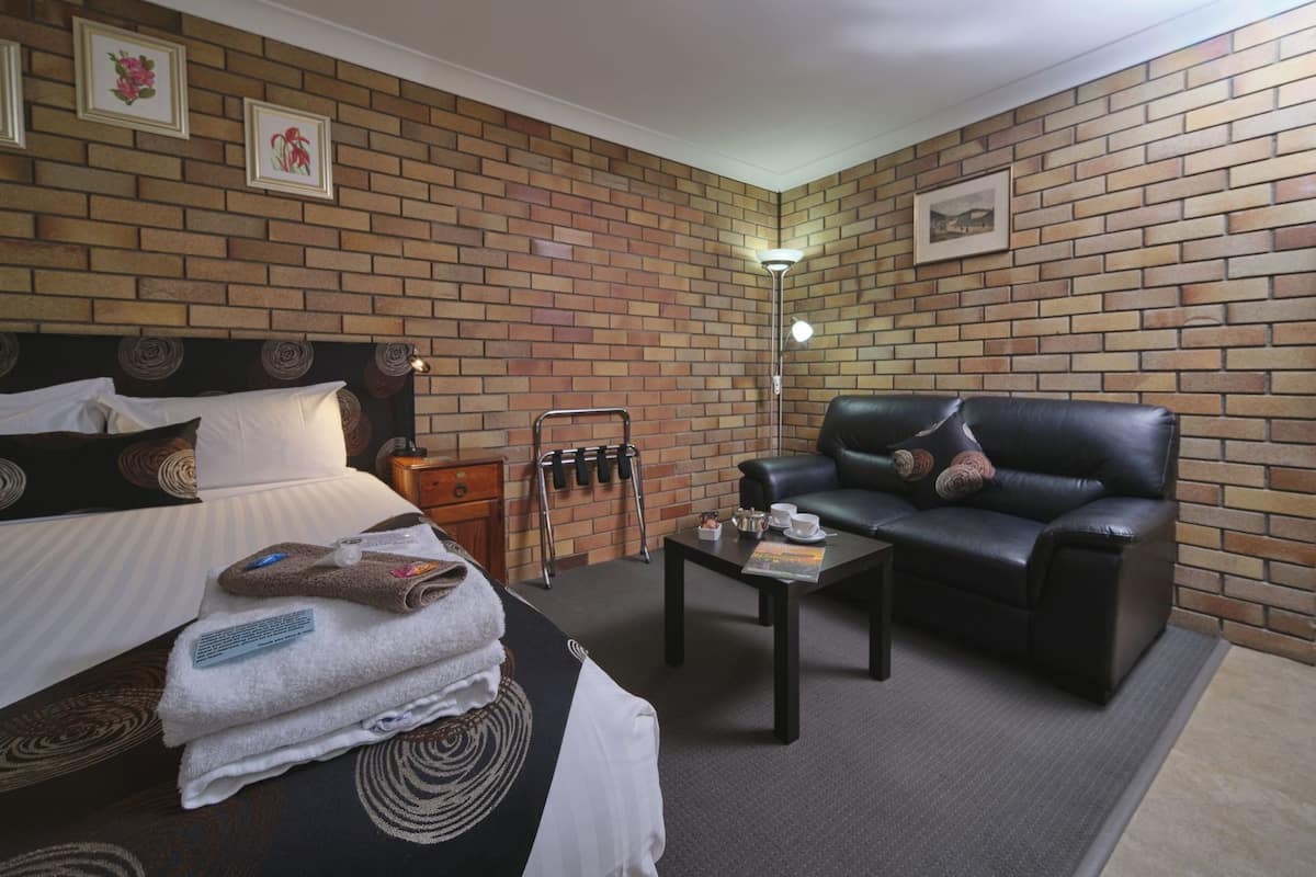 Habitación de hotel con pared de ladrillo, cama con cabecera, sofá de cuero negro, una mesita con lámpara y un perchero.