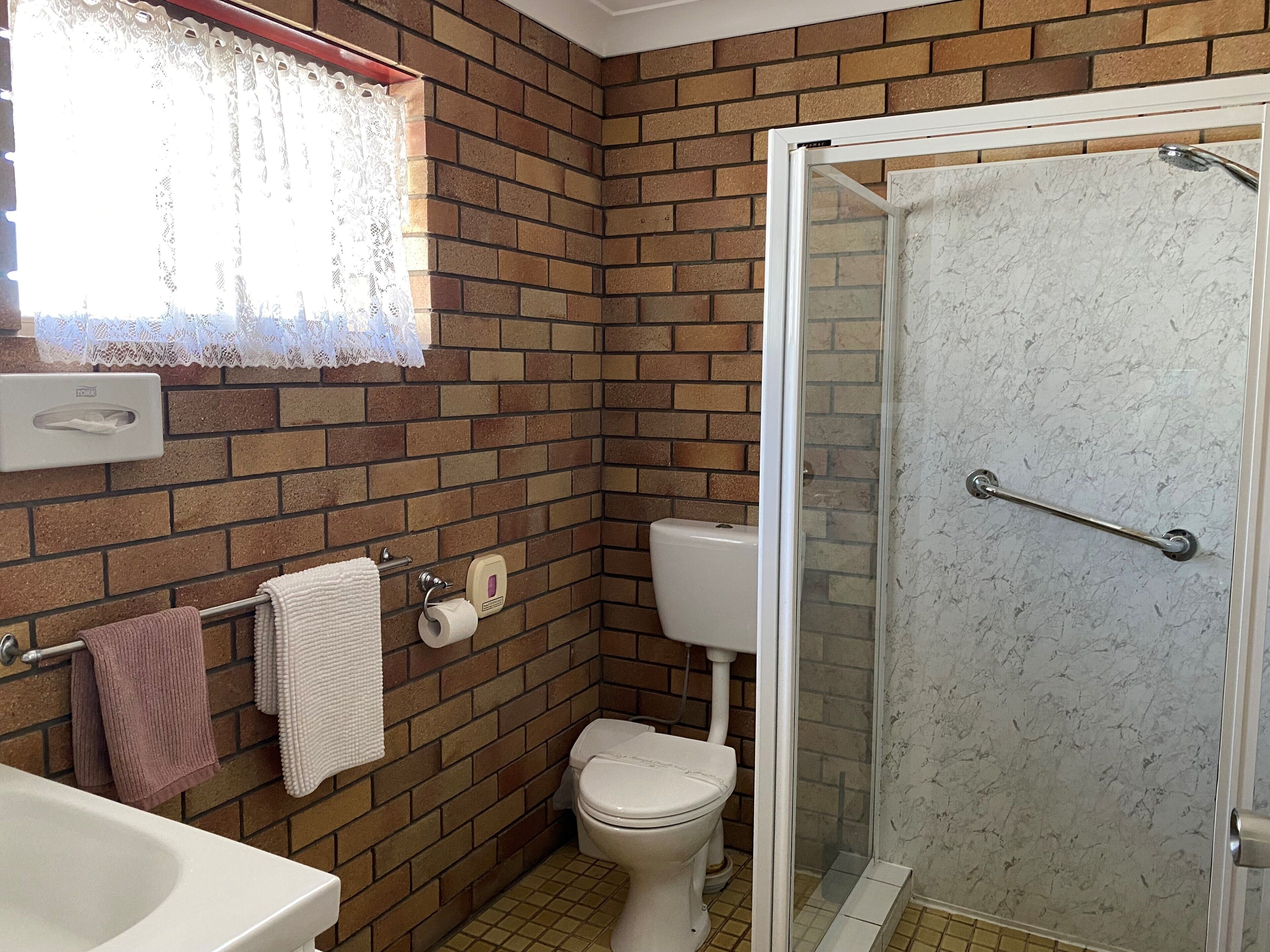 Un baño con pared de ladrillo, inodoro, ducha con puerta de cristal y lavamanos.