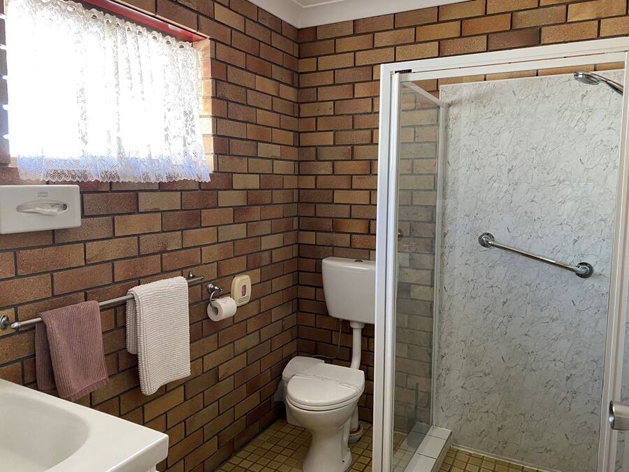 Un baño con pared de ladrillo, inodoro, ducha con puerta de cristal y lavamanos.