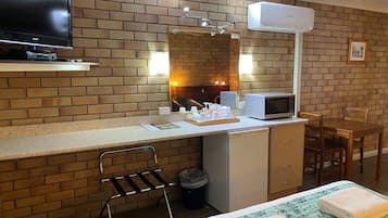 Habitación de hotel compacta con pared de ladrillo, televisor de pantalla plana, microondas, una pequeña mesa de comedor y cama con colcha estampada.