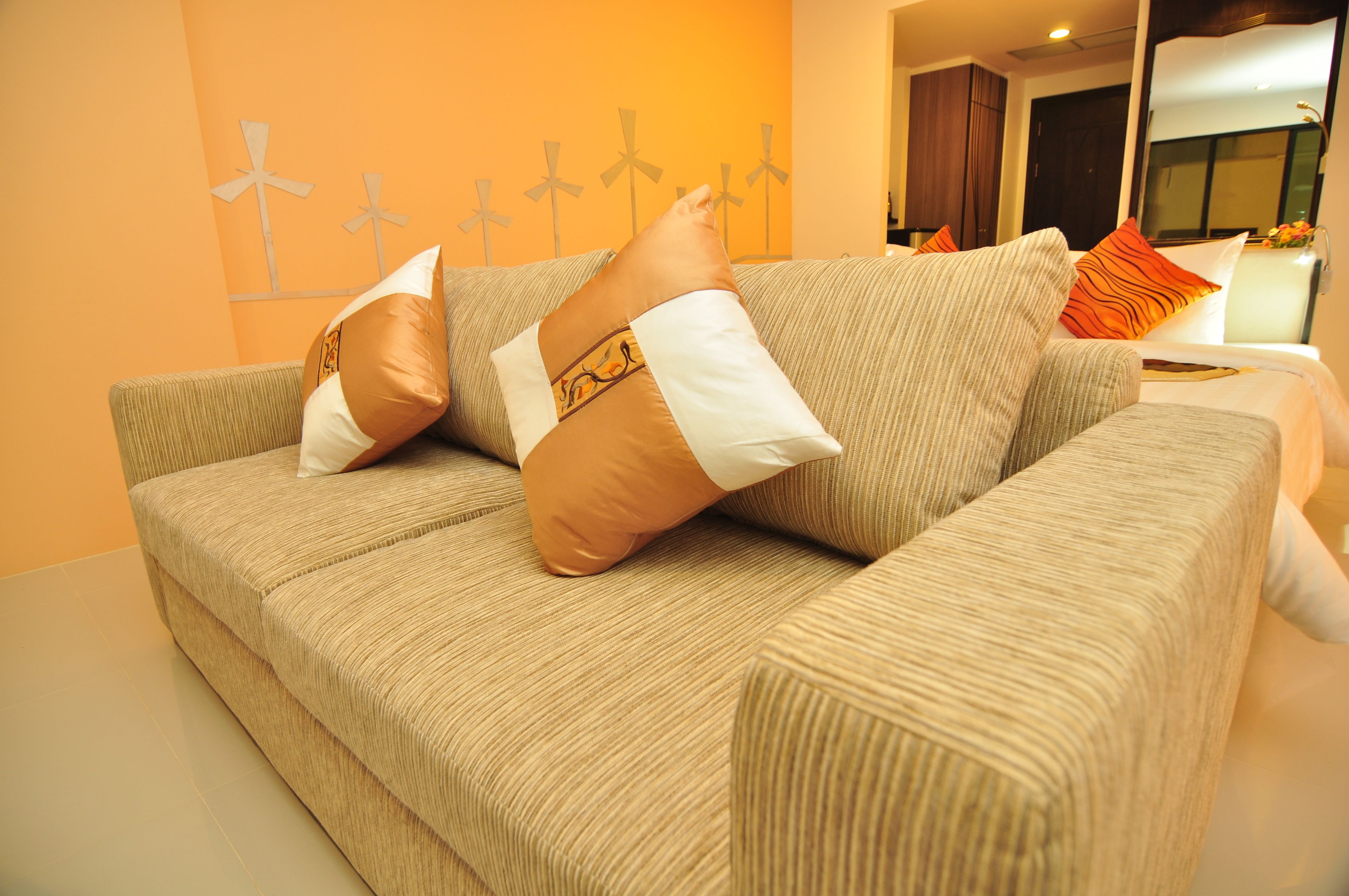 Un canapé beige agrémenté de coussins à motifs, dans une pièce dont un mur est orange et qui est décorée de moulins à vent.