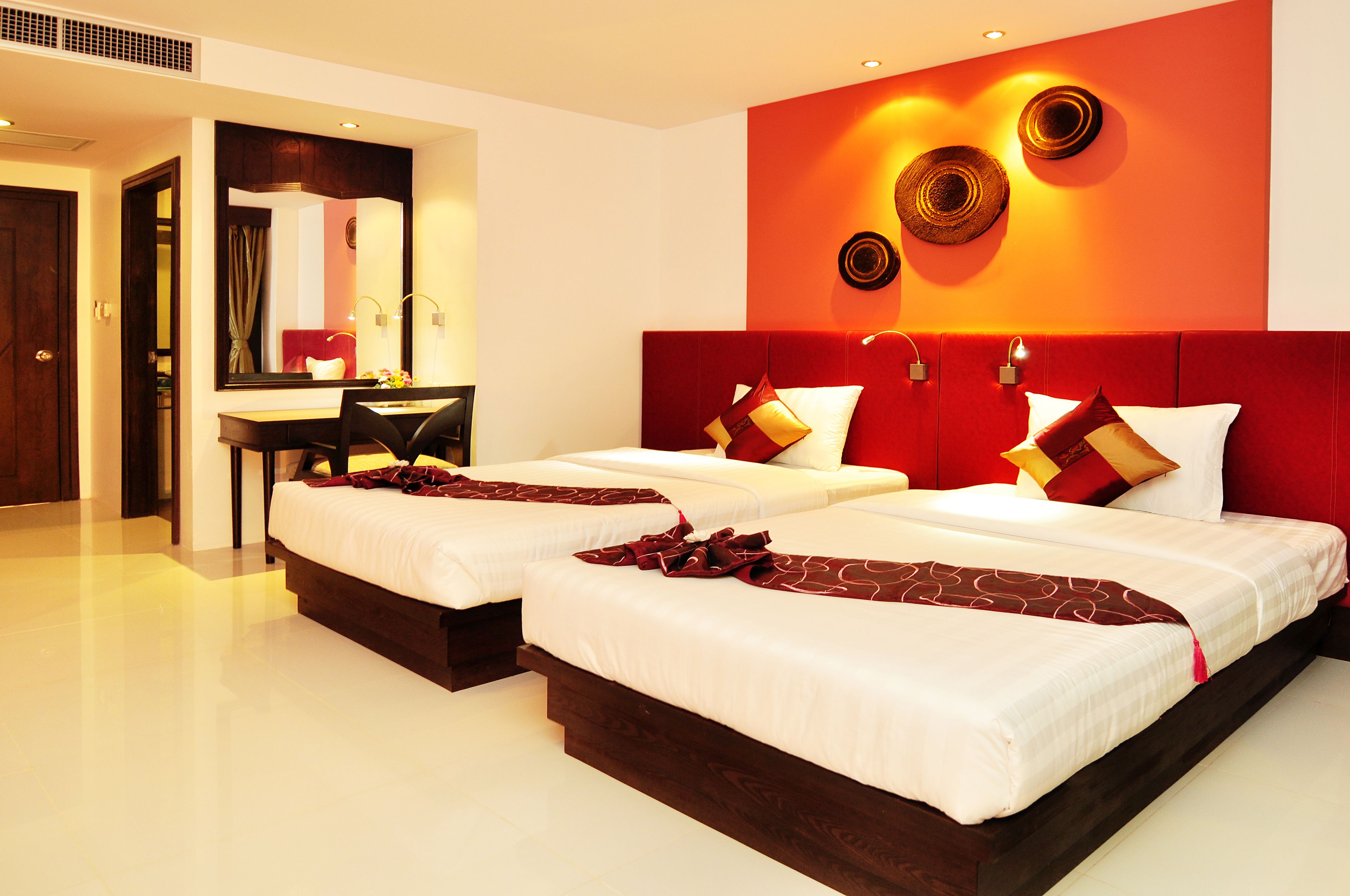 A hotel room with two beds, a desk, and a mirror.