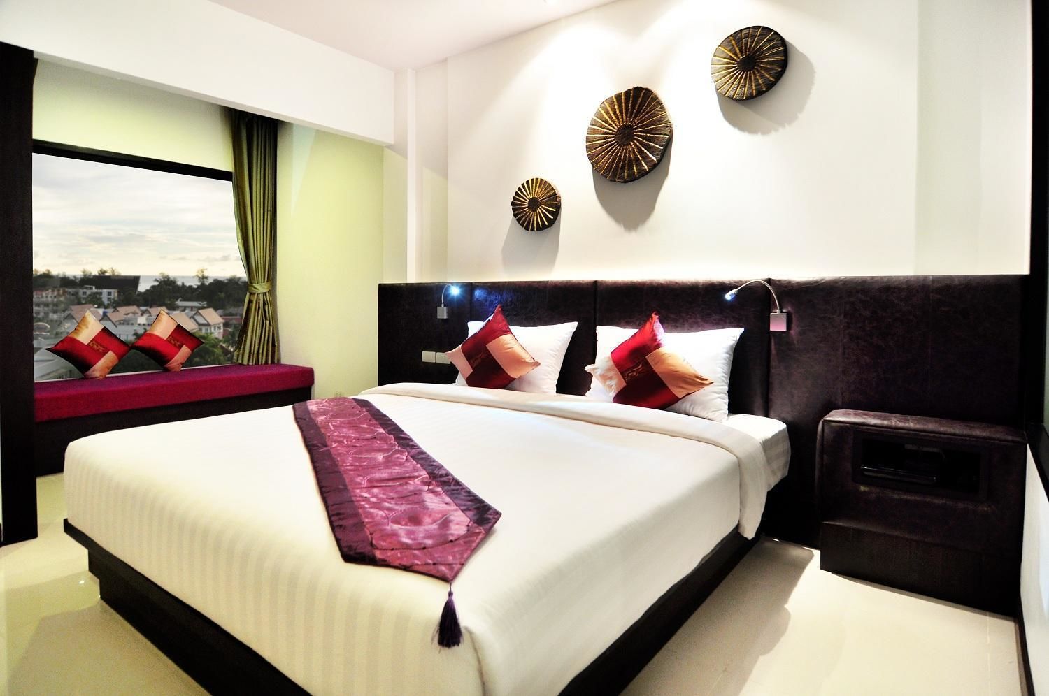A modern hotel room with a large bed, a nightstand, and a view of the city through a window.