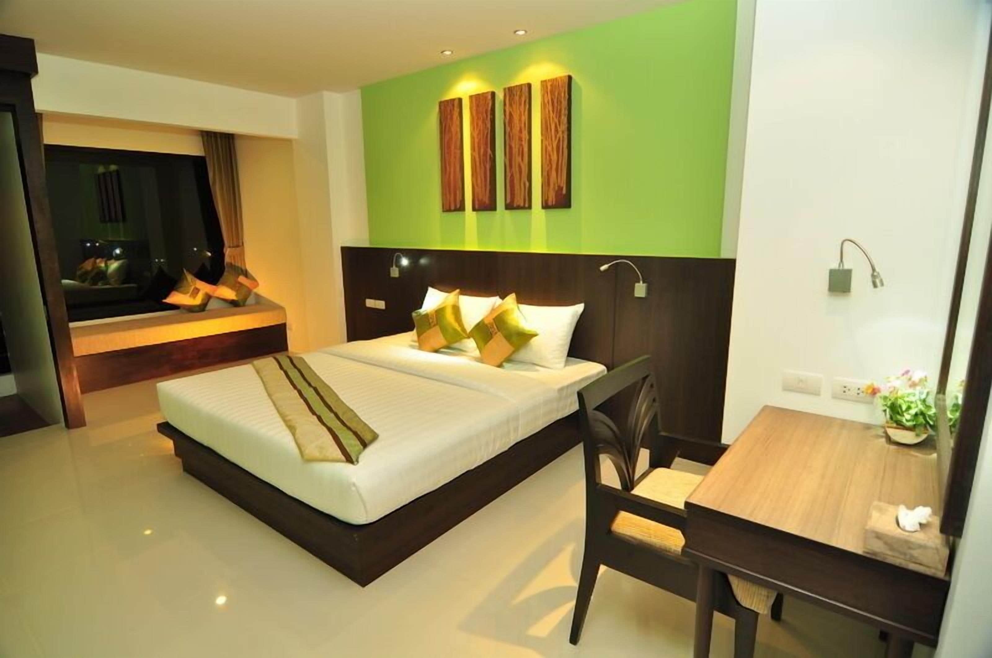 A modern hotel room with a large bed, a desk, and a green accent wall.