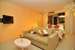 Una sala de estar moderna con un sofá color beige, una mesita redonda con un florero y un televisor de pantalla plana montado en la pared.