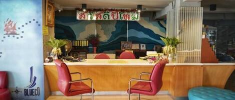 A reception area with a wooden counter, two red chairs, a blue cushioned bench, and a wall with a map and a sign.