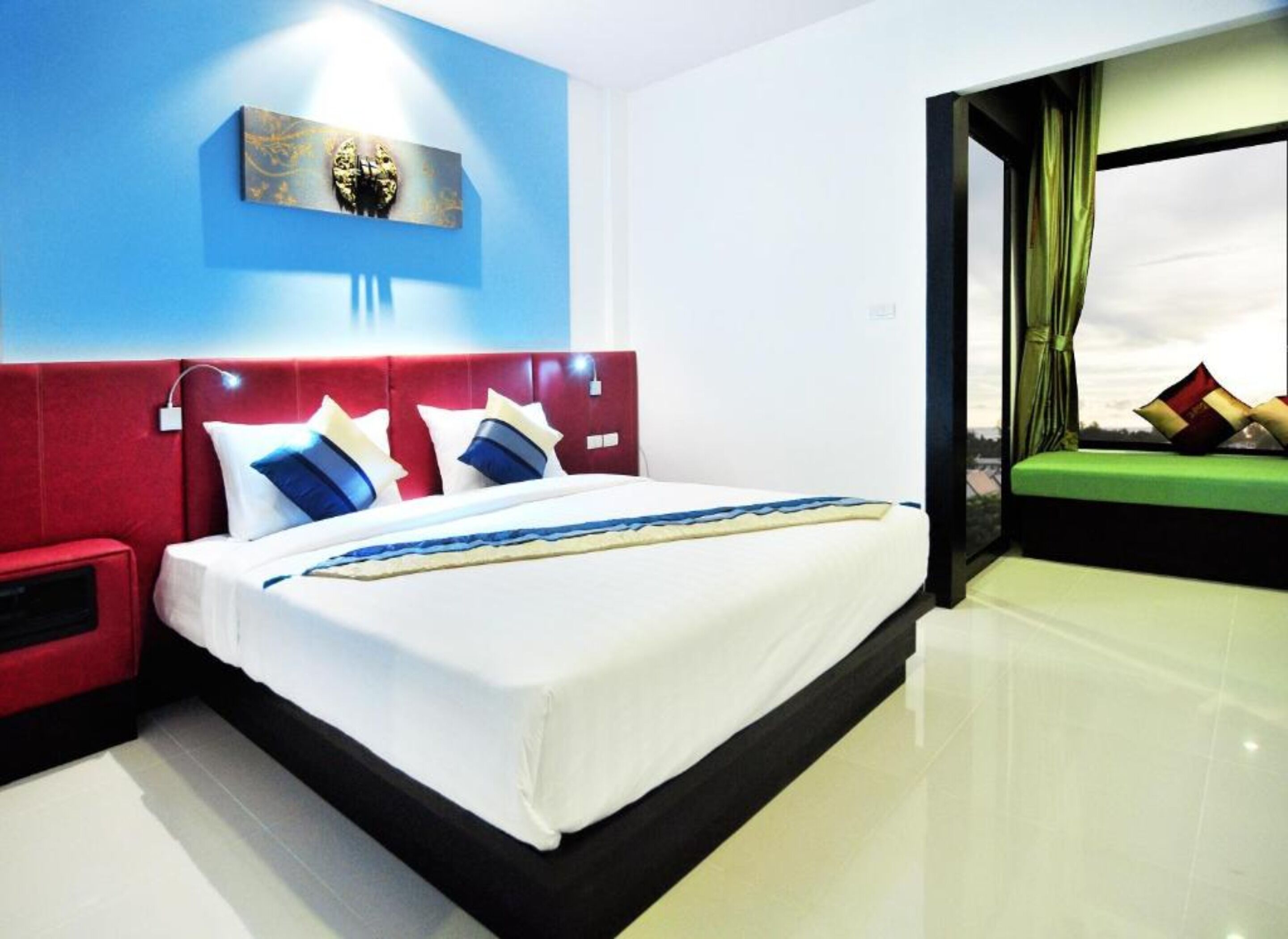 Une chambre d’hôtel moderne avec un grand lit, une tête de lit rouge et une vue sur le ciel par la fenêtre.
