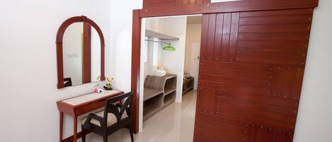 Una habitación con un escritorio de madera, una silla y un espejo. Se observa un armario con espejo y perchero.