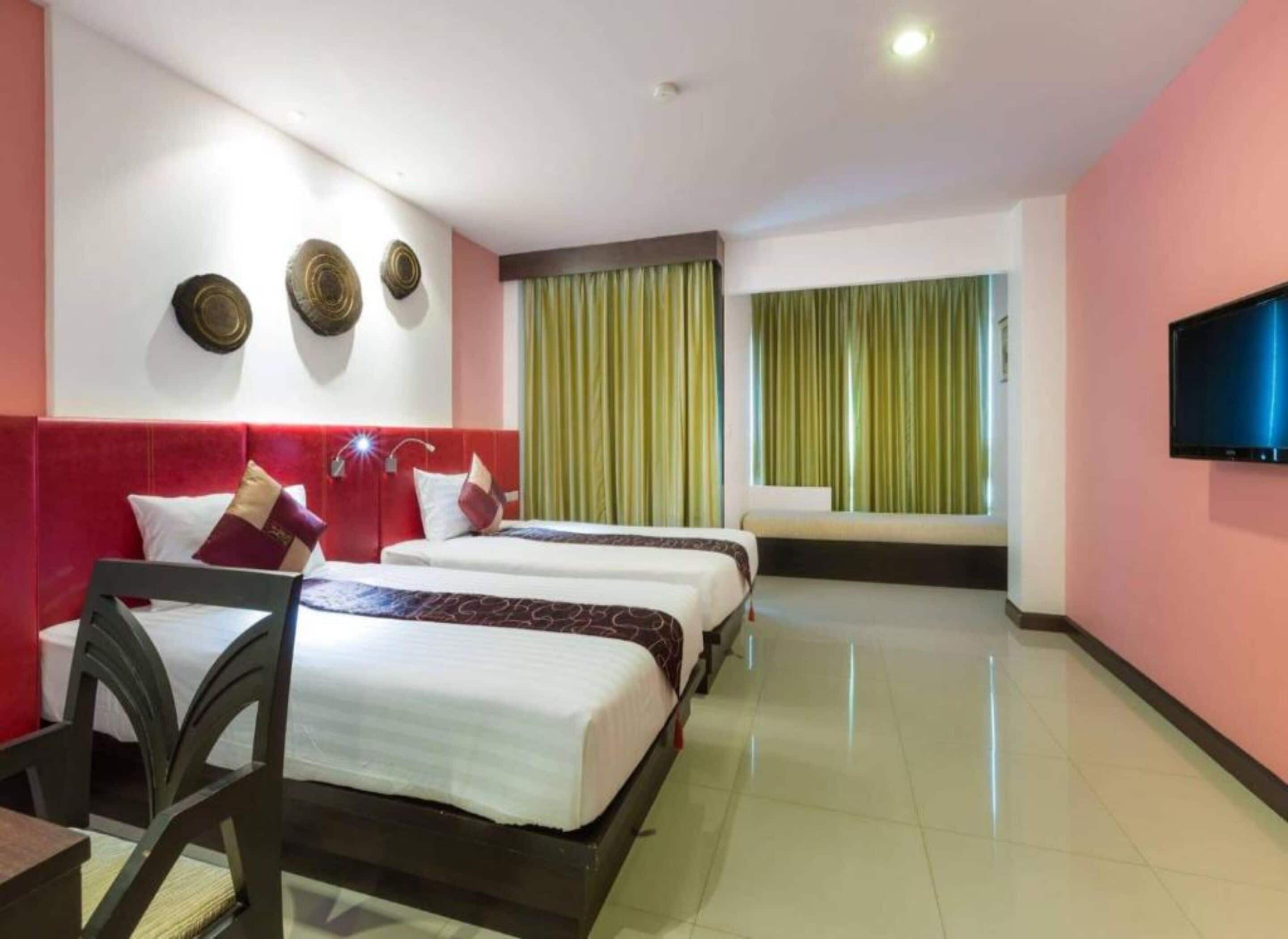 A hotel room with two beds, a TV, and a window with green curtains.