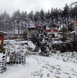 A hotel with a red and white exterior, surrounded by snow-covered trees and a garden. - Mount Paradise Nature Stay (Baluwapati Deupur)
