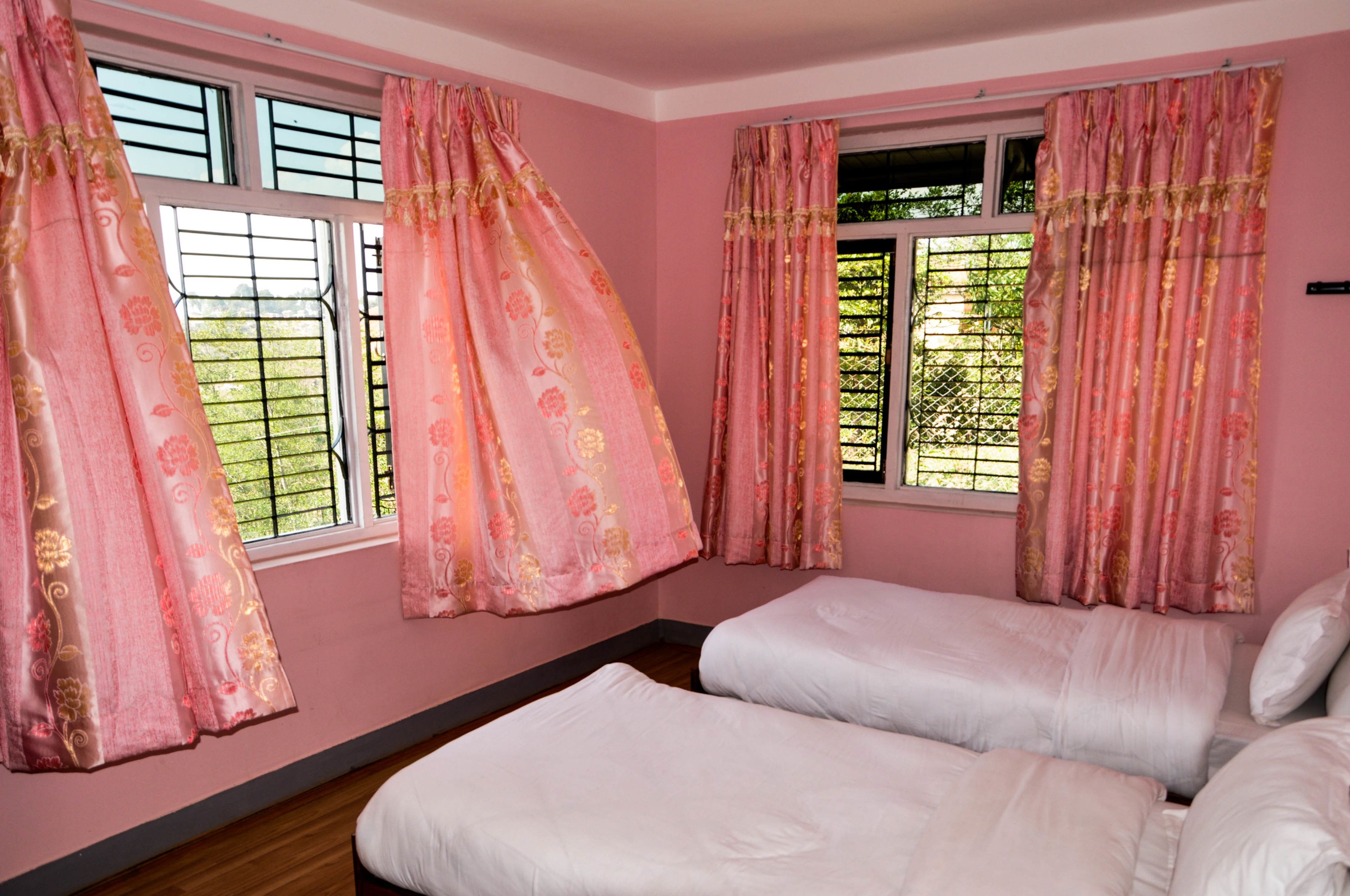 A bedroom with two beds, pink walls, and floral curtains.