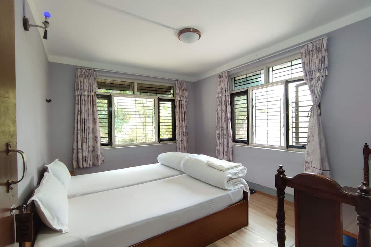 A single bed with white linens, two windows with shutters, a ceiling fan, and a wooden headboard.