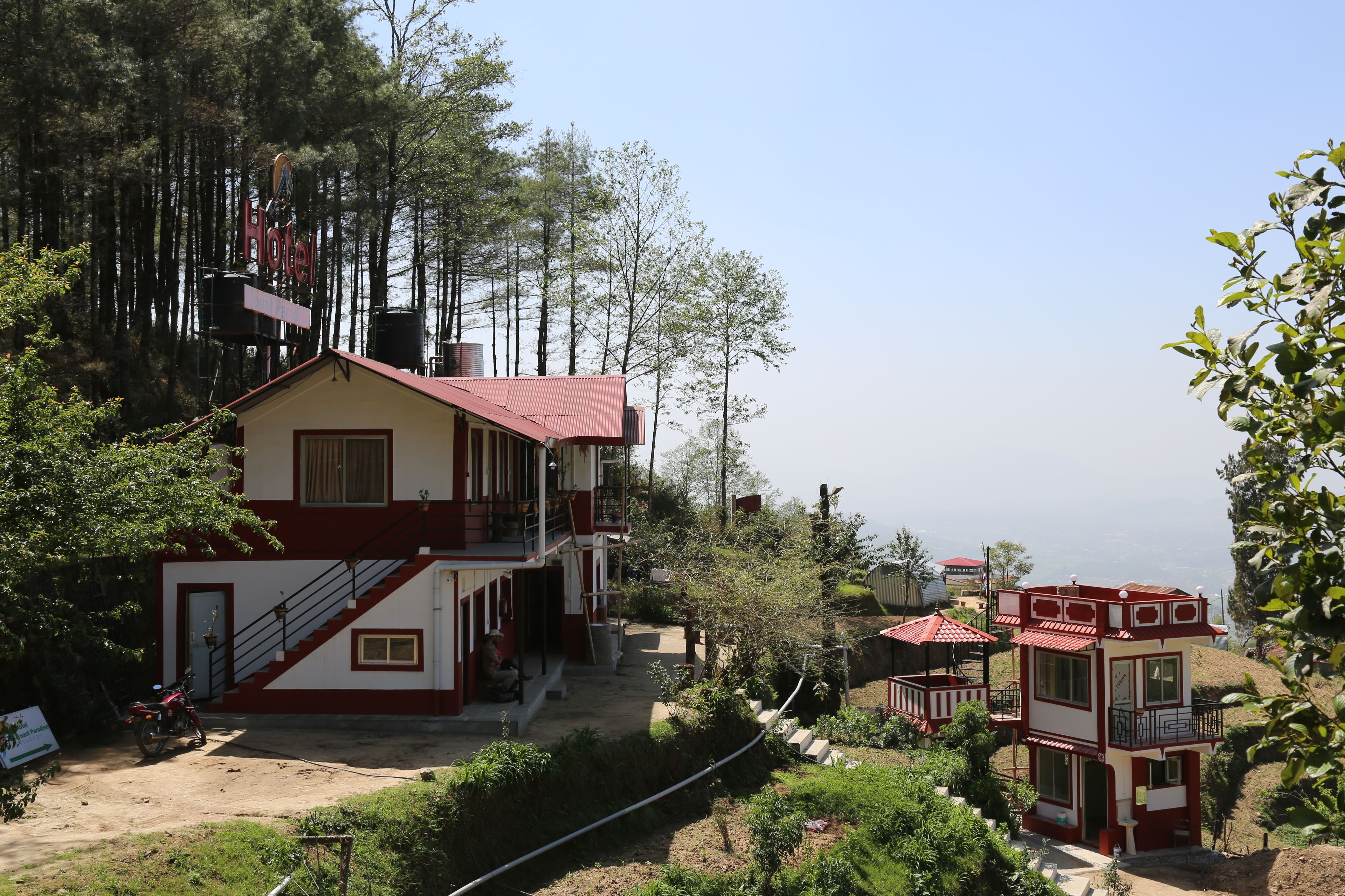 A two-story hotel with a red roof, a staircase leading to the upper floor, and a view of the surrounding forest.