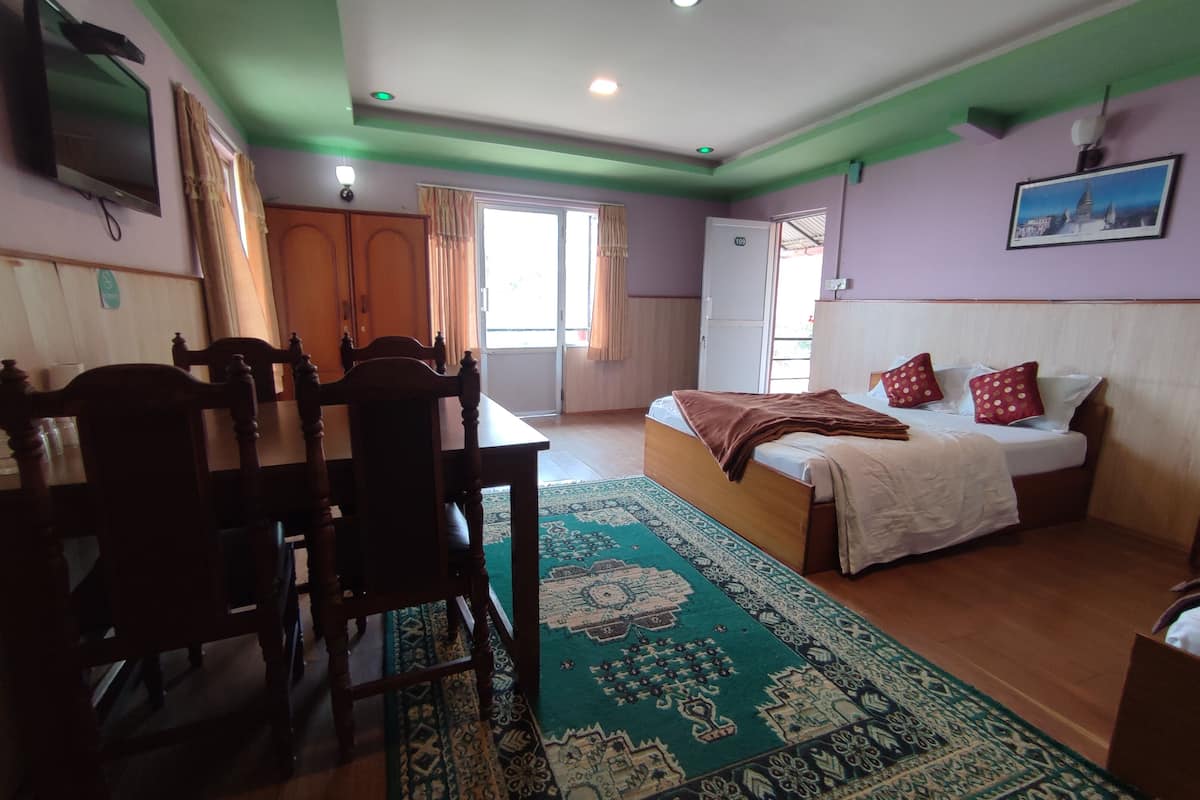 A bedroom with a bed, a desk, a chair, a TV, and a window with curtains.