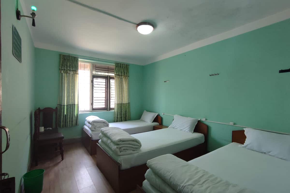 A room with three beds, a window with curtains, a ceiling fan, and a green bucket on the floor.